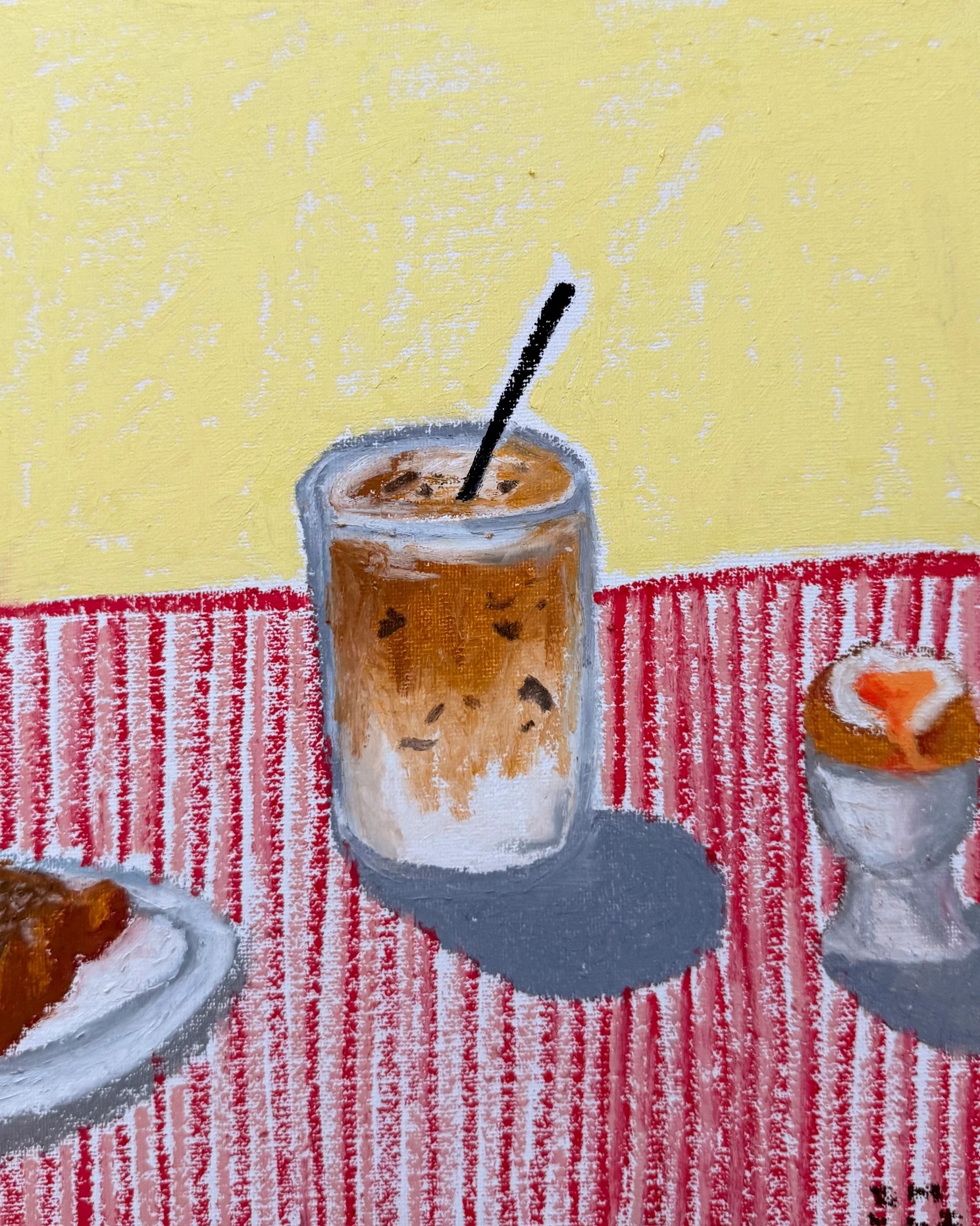 Iced coffee in a glass with an egg and croissant on a red and white striped tablecloth